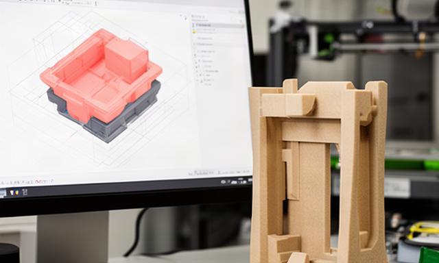 Bildschirm mit 3D-CAD-Modell neben einem 3D-gedruckten Verpackungseinsatz im Entwicklungsraum